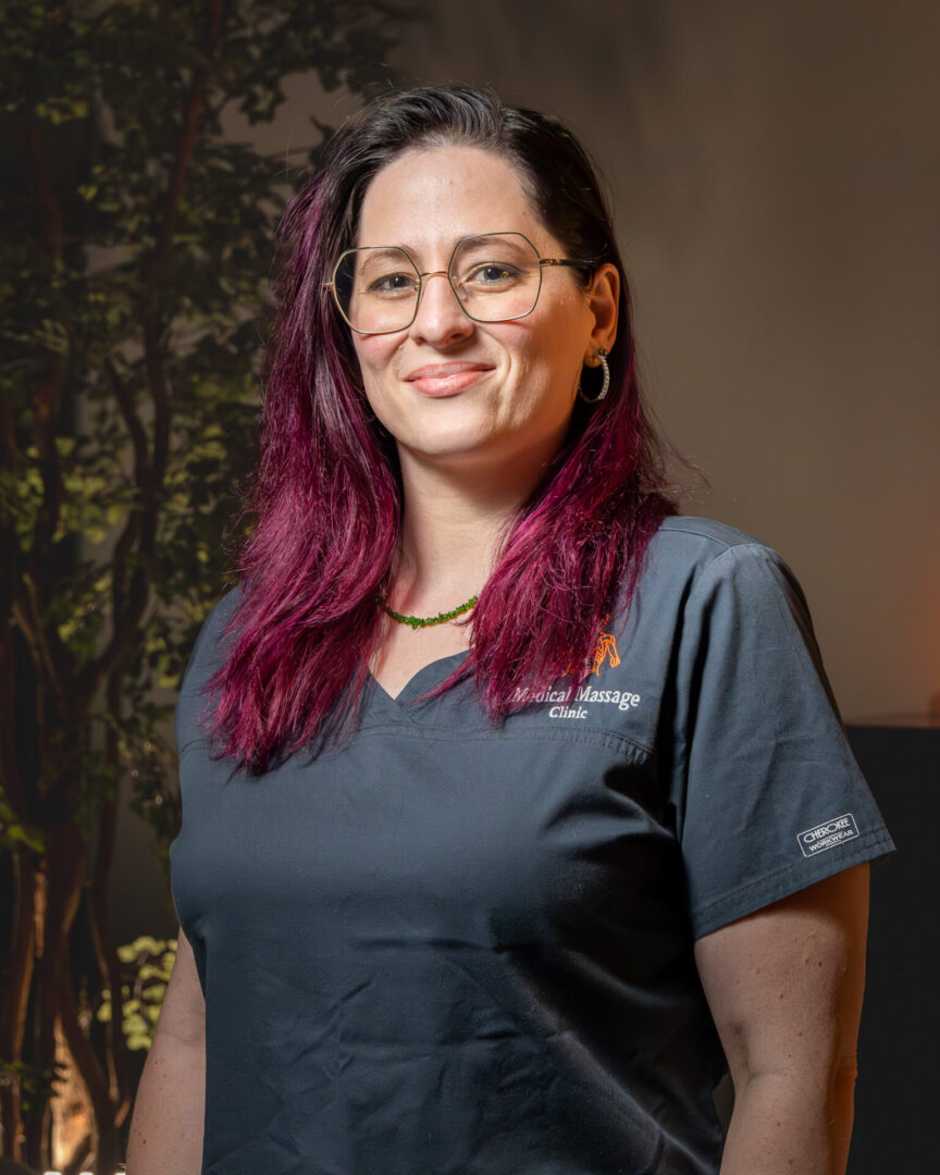 A woman with purple hair standing in front of trees.