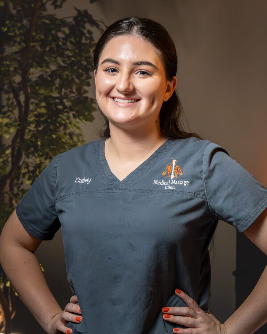 A woman in grey scrubs standing next to a tree.